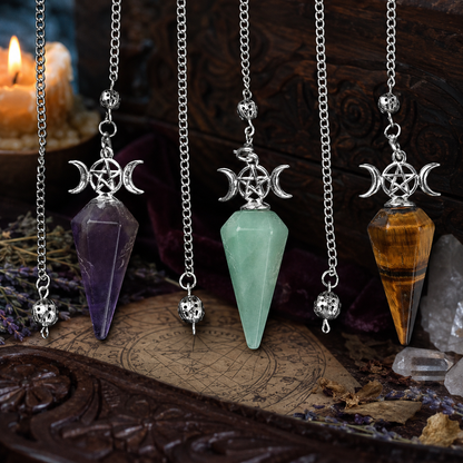 Amethyst green aventurine and tiger eye Triple Moon pendulums on a Wiccan altar